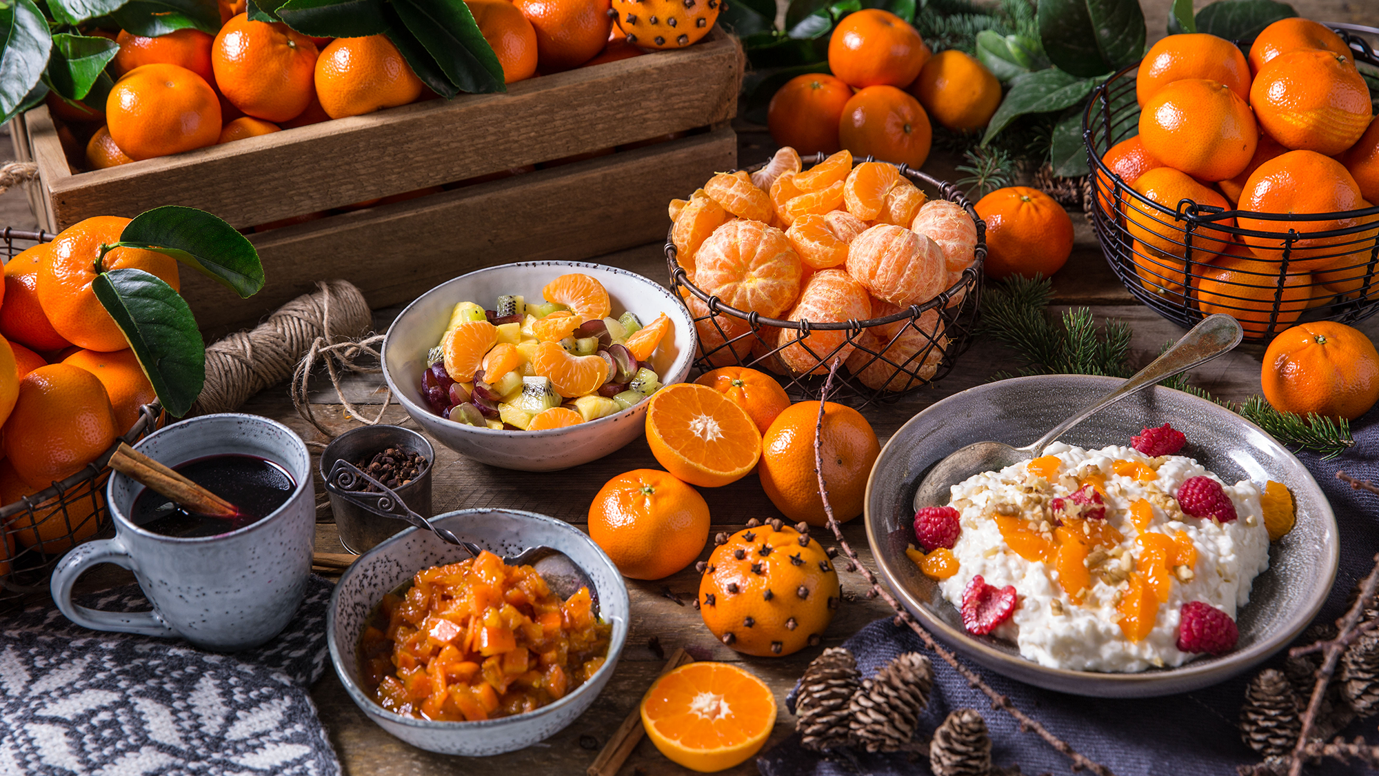 Et utvalg av klementiner, en kopp med kaffe, og ulike desserter på et bord med grønne blader og små gule frukter.
