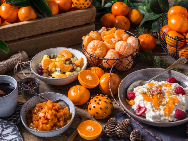 Et utvalg av klementiner, en kopp med kaffe, og ulike desserter på et bord med grønne blader og små gule frukter.