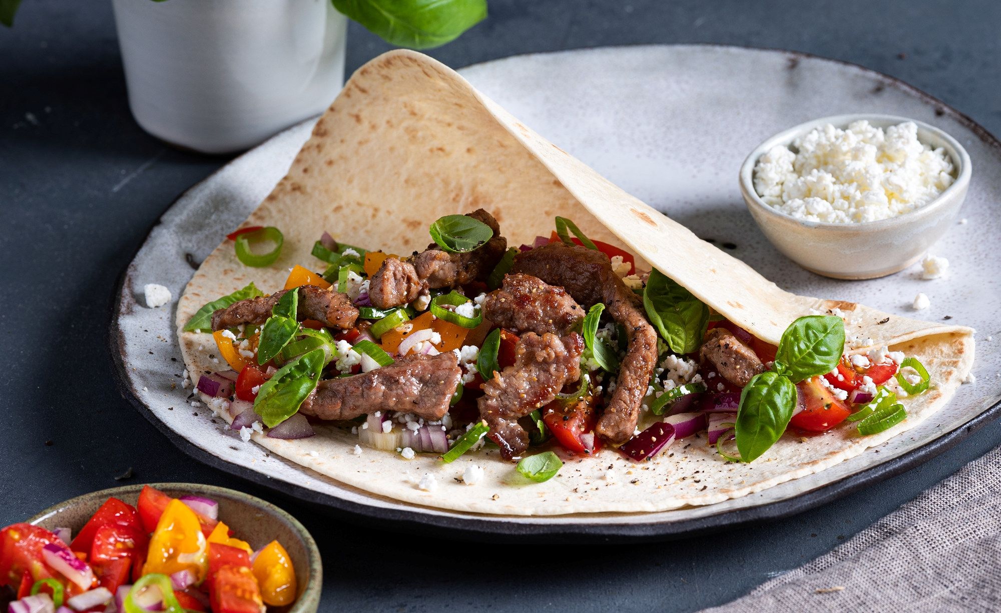 Strimler av fersk lammelår i en tortilla med grønnsaker og en skål med hvit saus ved siden av