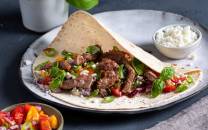 Strimler av fersk lammelår i en tortilla med grønnsaker og en skål med hvit saus ved siden av