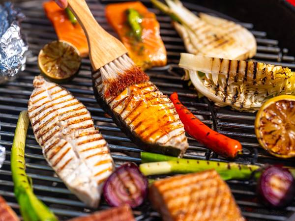 Fisk og skalldyr grillet på grill med grønnsaker som chili og løk, og sitroner i bakgrunnen.