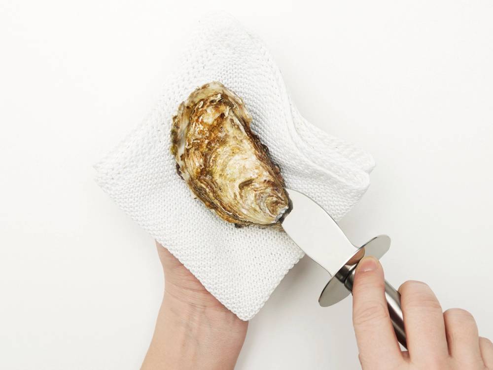 En person holder en østers med en klut og en liten kniv, klar til å åpne den.