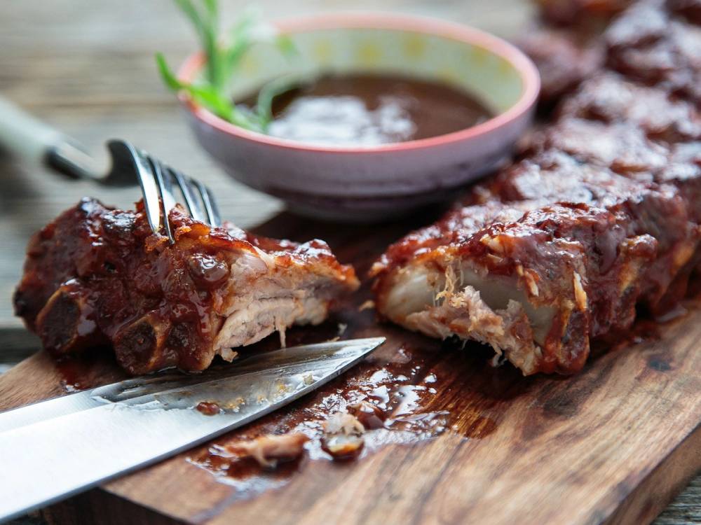 Spareribs med fiken på et skjærebrett, med en kniv og en skål med saus i bakgrunnen.