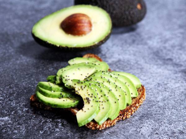 Skive av avokado på grovt brød med chiafrø, med en hel avokado i bakgrunnen.