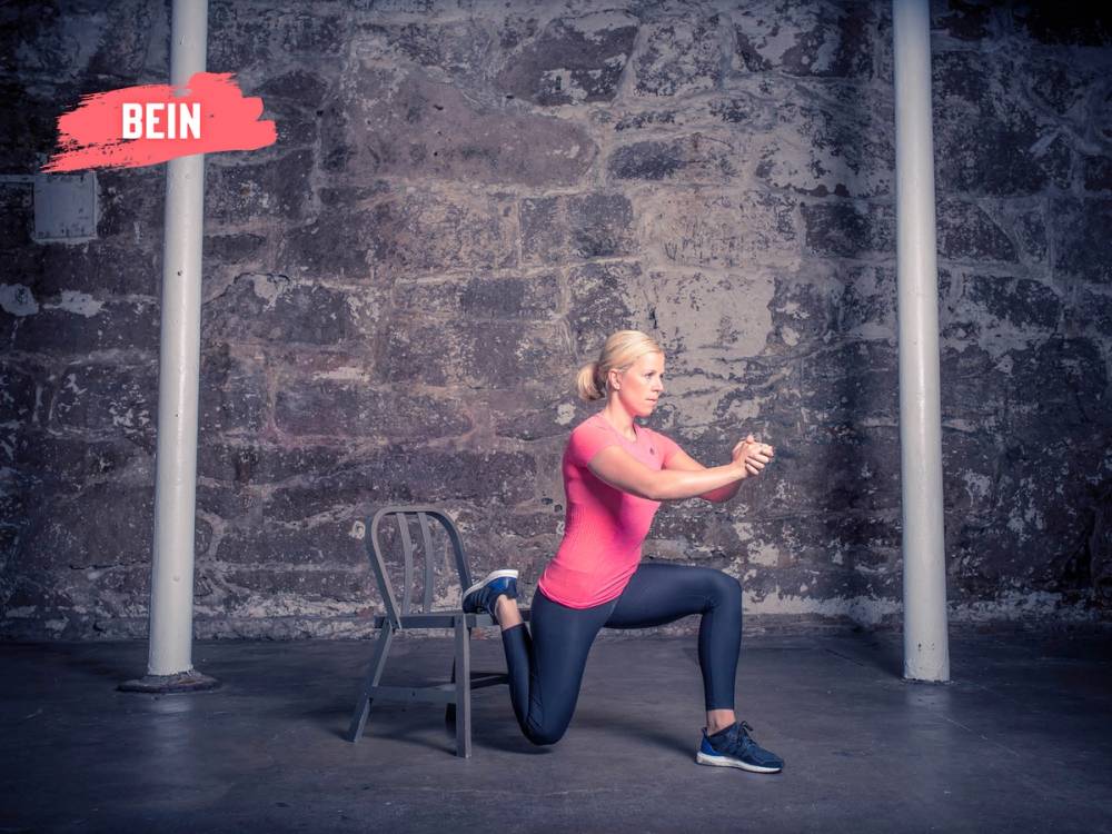 Person utfører en splitknebøy med ett bein på en stol og det andre på gulvet, foran en murvegg.