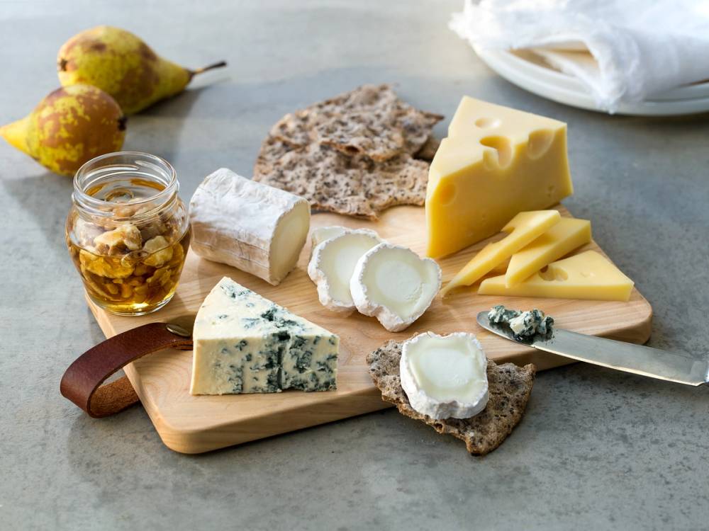 Et lite ostefat med blåmuggost, chèvre, gul ost, kjeks og et glass med honning eller syltetøy, plassert på et trebrett.