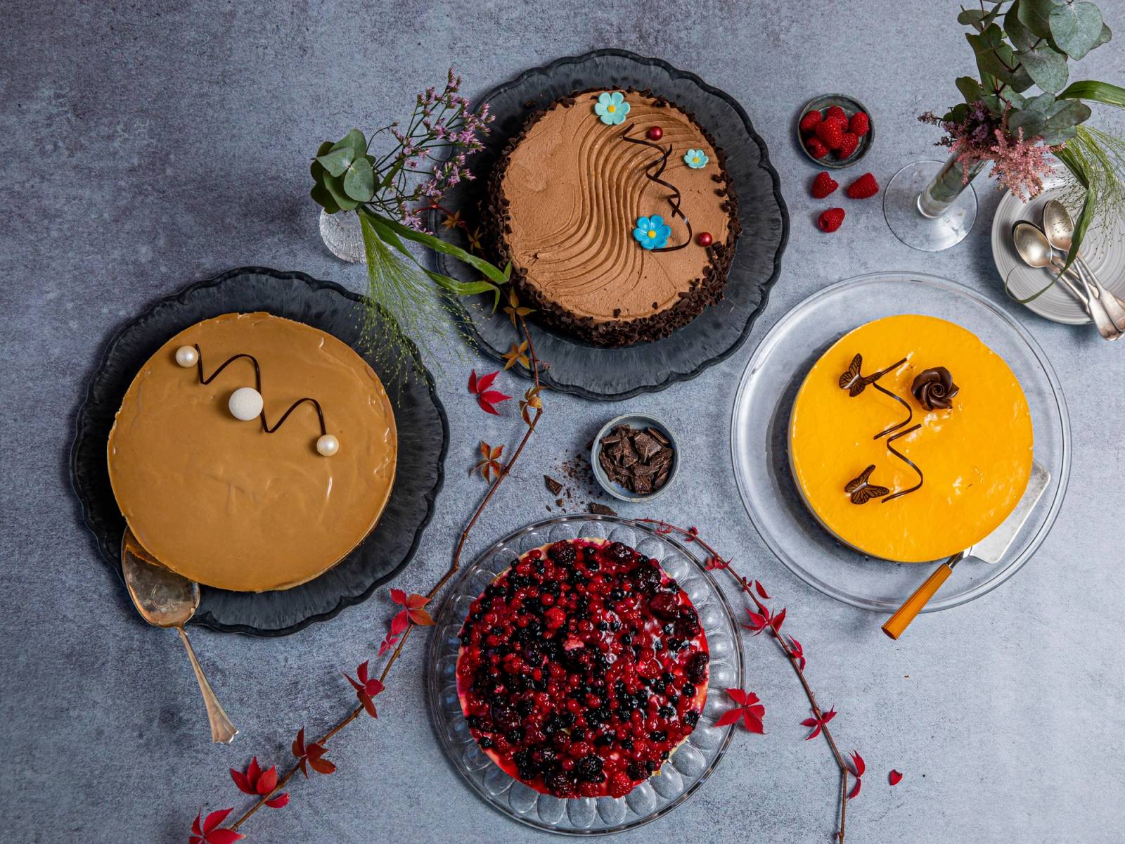 Tre kaker og en skål med bær på et bord, omgitt av blomster og dekorasjoner.