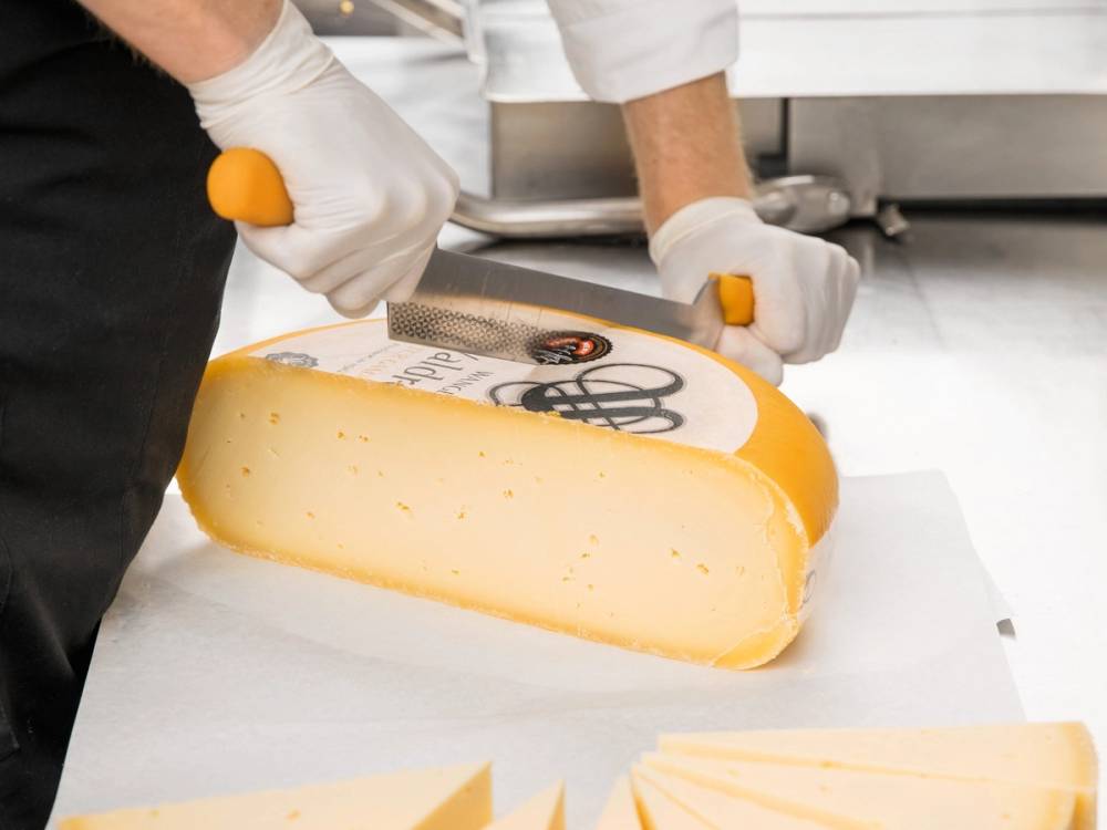 Person skjærer i en stor blokk med gul ost på et kjøkkenbord.