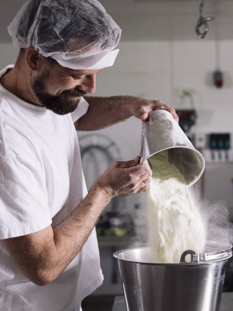 En person heller iskrem fra en bøtte inn i en stor metallbolle på et kjøkken.