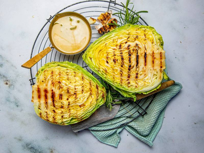 Grillet spisskål med urtesmør og en liten skål med saus på et fat med en gaffel ved siden av.