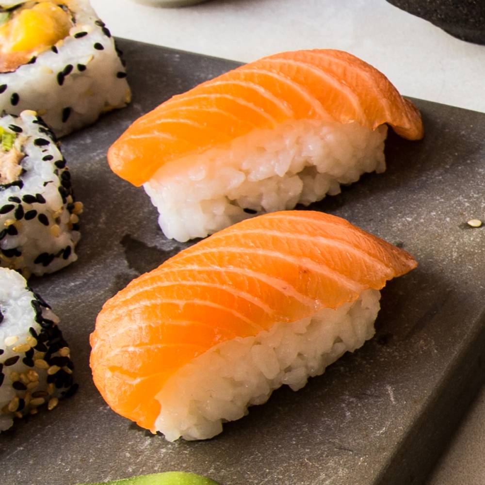To nigiri med skiver av laks på ris, plassert på en svart tallerken.