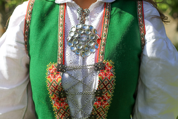 Nærbilde av en person som har på seg en grønn bunadsskjorte med broderte detaljer og et sølvbelte, med en hvit skjorte under.