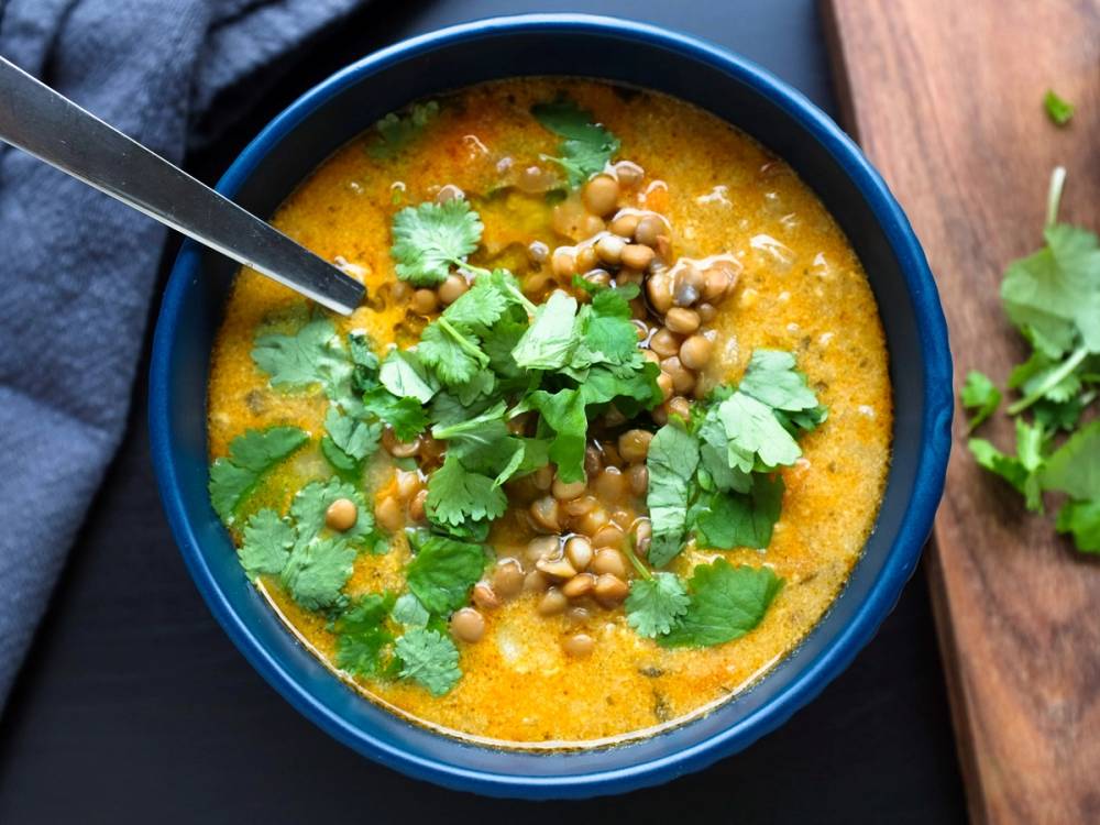 Kyllingsuppe med linser og frisk koriander i en blå skål på et bord.