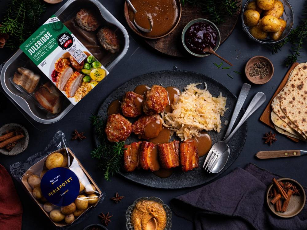 Juleribbe med tilbehør som poteter, saus og grønnsaker på et svart bord