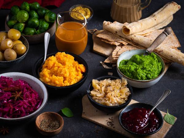 Ulike tilbehør til julemat, inkludert grønne lime, poteter, gulrotmos, surkål, flatbrød, og ulike sauser, på et bord.