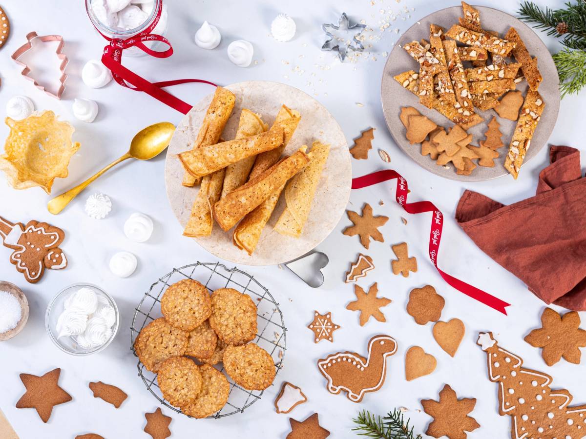 Julebakst med pepperkaker, kokosmakroner og småkaker på et bord med julepynt og dekorasjoner.