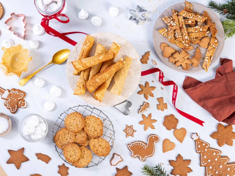 Julebakst med pepperkaker, kokosmakroner og småkaker på et bord med julepynt og dekorasjoner.