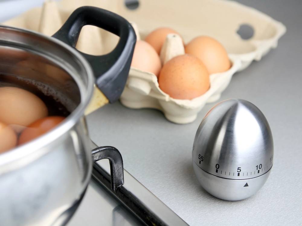 Egg i en åpen eggkartong med en kjele på komfyren i bakgrunnen.