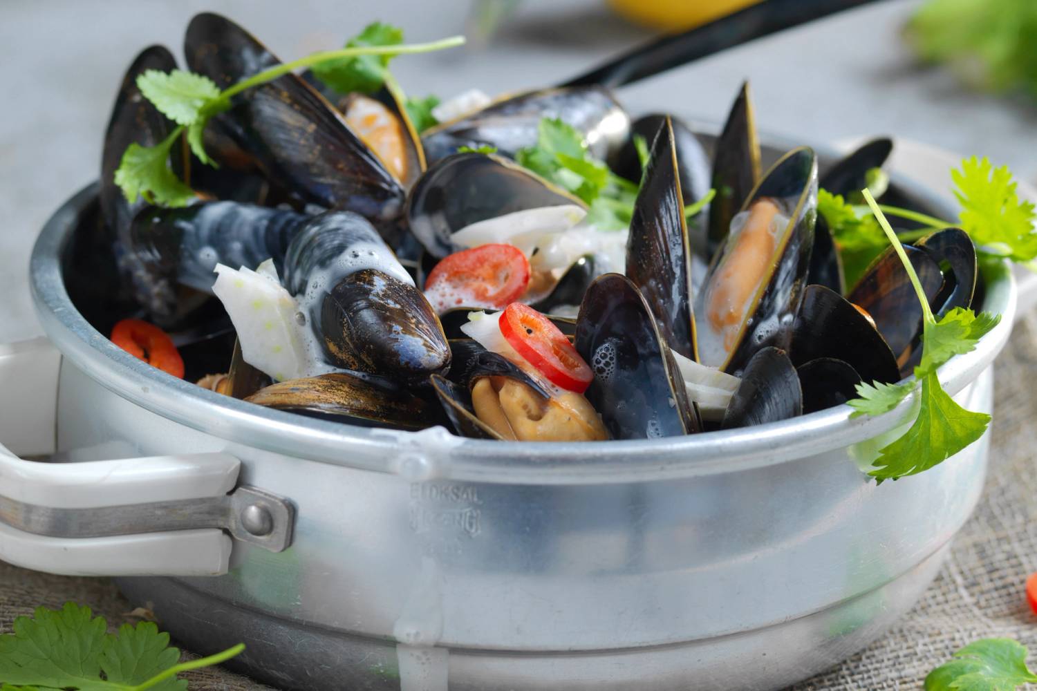 Asiatiske blåskjell i en metallbolle med grønne urter og tomater, klar til servering.