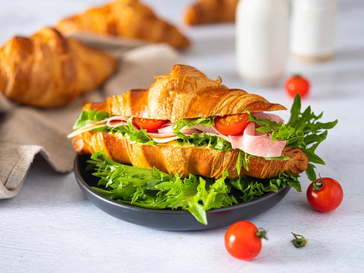Croissant fylt med skinke, ost, salat og tomater på en tallerken.