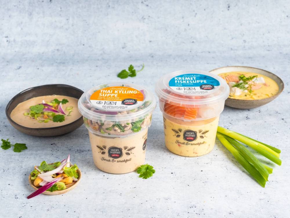 To porsjoner med ferdiglaget suppe i plastkopper, omgitt av grønne vårløk og en liten salat, på en lys bakgrunn.