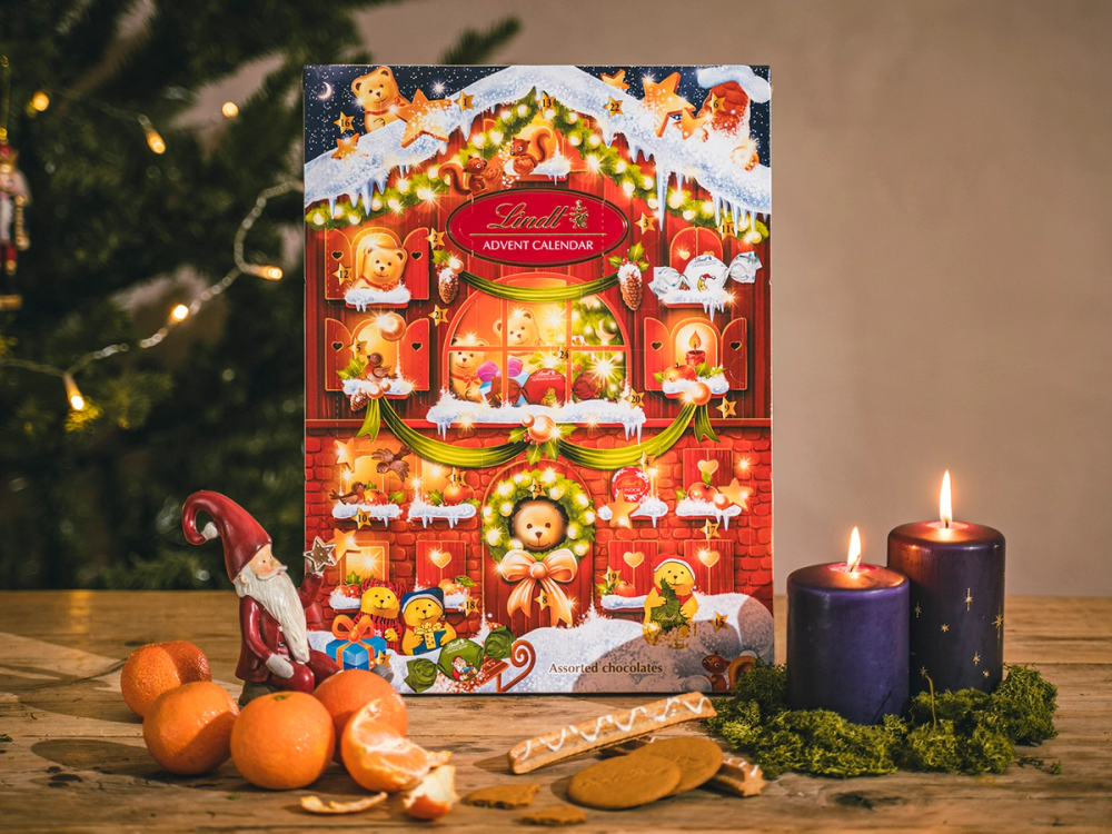 Et julekalender med julemotiver står på et bord med lyslenker, lys og små gresskar foran.