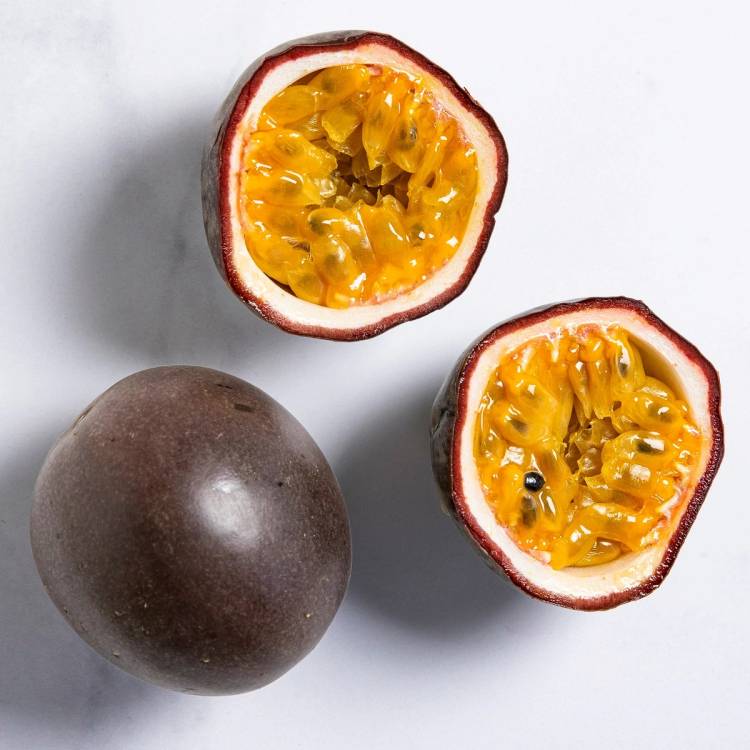 To halverte pasjonsfrukter med gul fruktkjøtt og svarte frø, og en hel pasjonsfrukt ved siden av på en hvit bakgrunn.