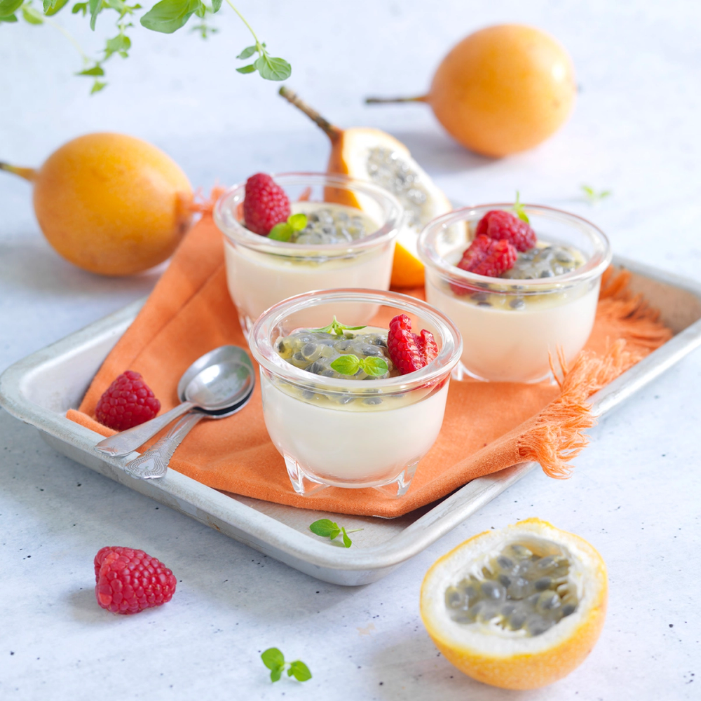 Pannacotta med granadilla og bær i små glass på et serveringsfat med en skje og frukt rundt.