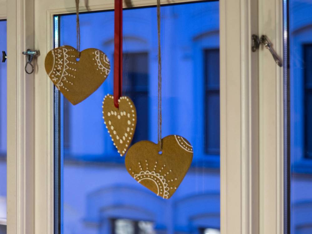 Tre gullfargede hjerteformede julepynt henger i et vindu med blå kveldshimmel utenfor.