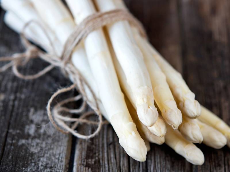 En bunt hvite asparges bundet sammen med en tråd på en treplate.