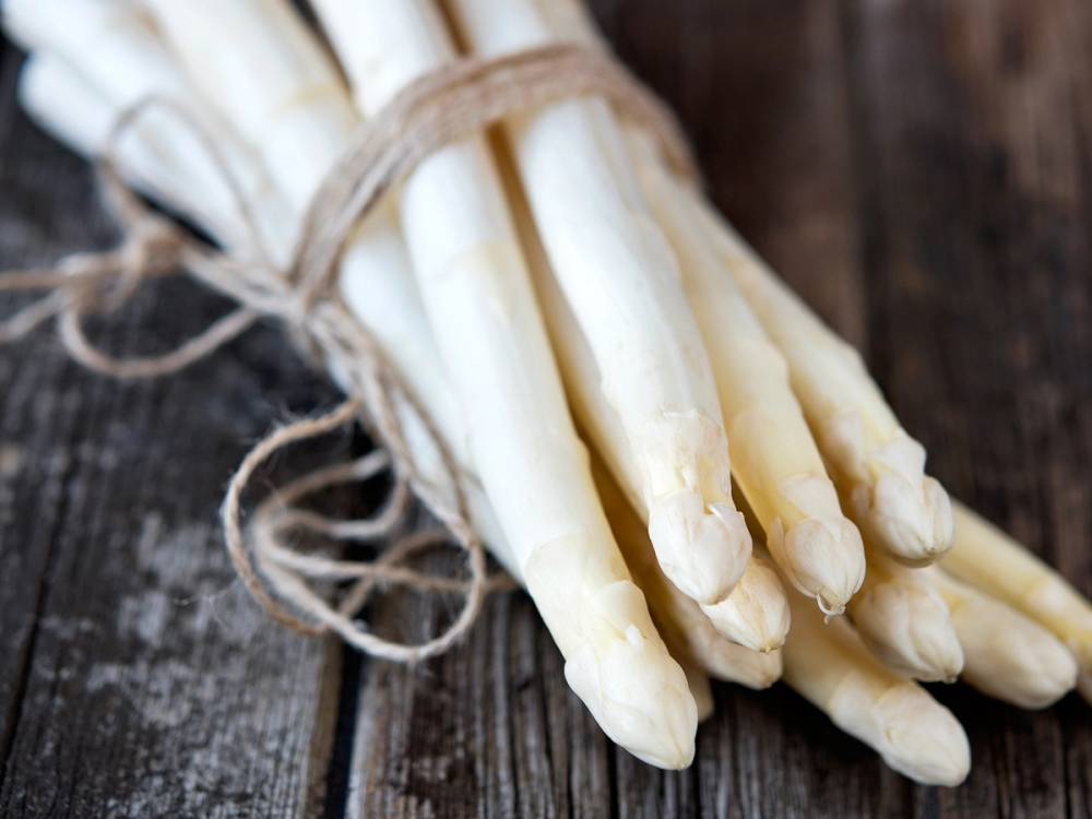 En bunt hvite asparges bundet sammen med en tråd på en treplate.