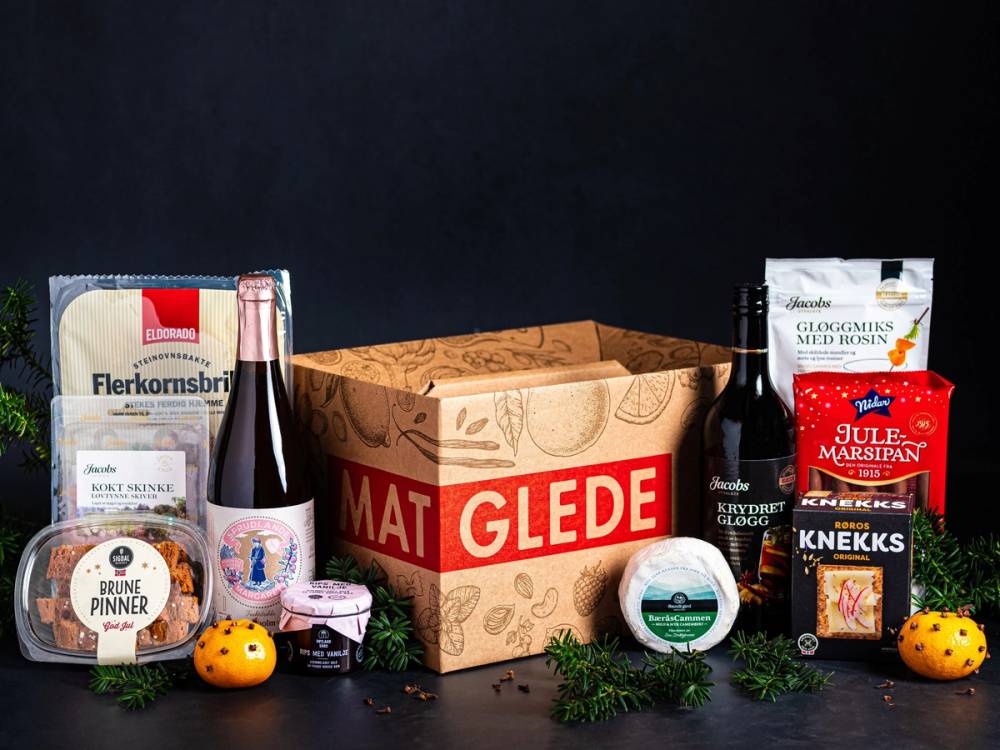 Gaveesker med ulike mat- og godteriprodukter for bedrift og privat, plassert på et bord med en åpen eske og noen små gaver rundt.