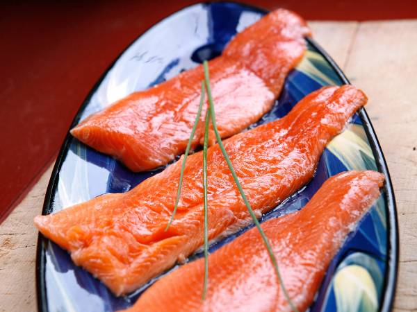 Fire skiver med røkt laks på en blå og hvit keramikkplate, pyntet med to tynne grønnkledde stilker.