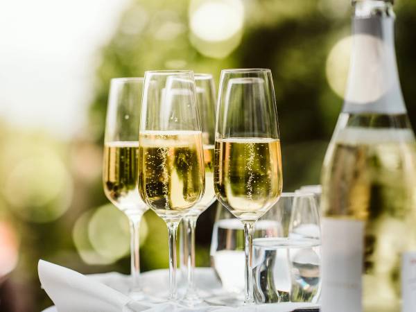Flere champagneglass med alkoholfri champagne på et bord utendørs med grønn bakgrunn