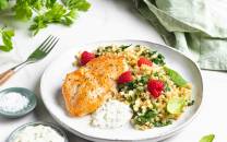 Kyllingfilet med blomkålris og friske bringebær på en hvit tallerken, omgitt av urter og små skåler med saus og krydder.