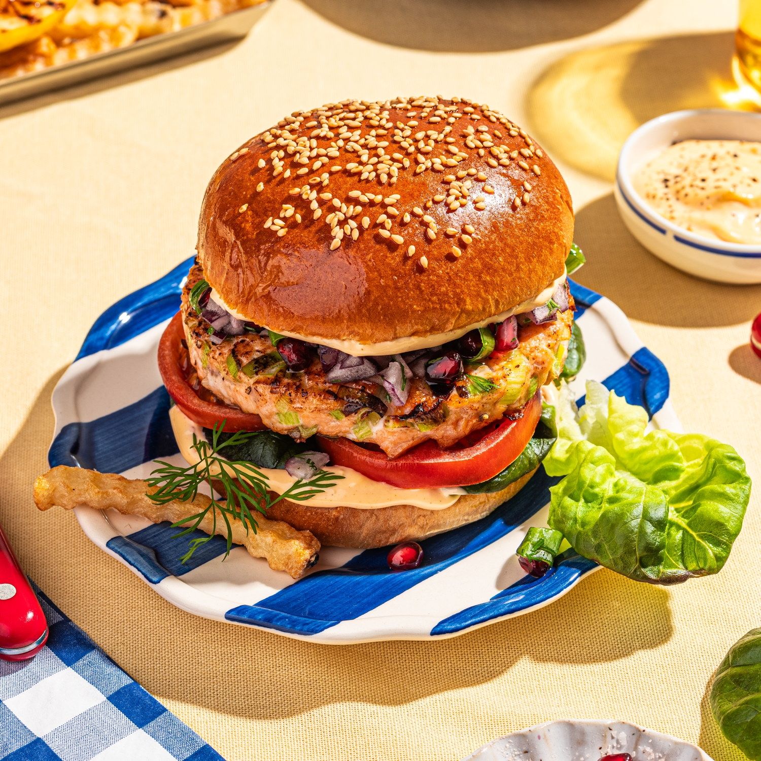 Lakseburger med granateple og grønnsaker på en tallerken, omgitt av tilbehør og drikke.