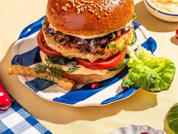 Lakseburger med granateple og grønnsaker på en tallerken, omgitt av tilbehør og drikke.