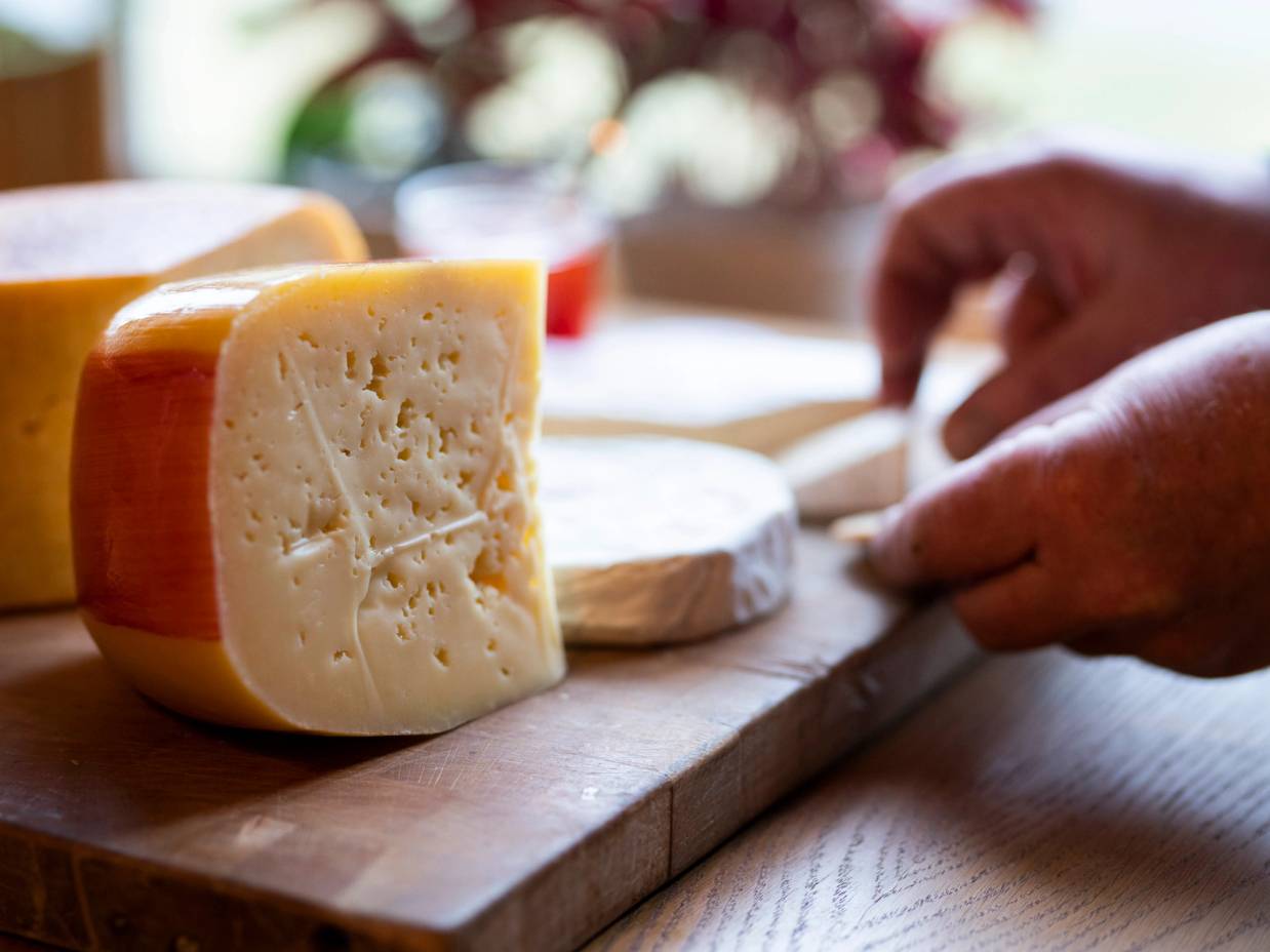 To typer ost på et skjærebrett med en person som skjærer ost i bakgrunnen.