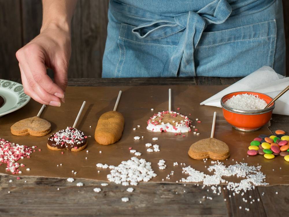 Person som lager jule- eller bursdagskaker med kjeks, kokos og fargerikt smågodt på et bord.