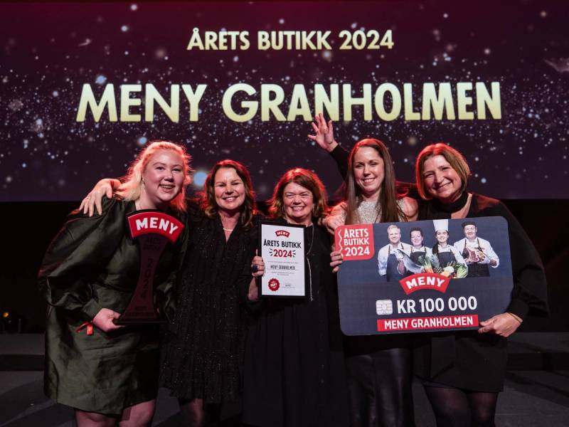 En gruppe mennesker holder opp en stor sjekk med teksten 'KR 100 000' og 'Meny Granholmen' under en banner som sier 'Årets butikk 2024'.