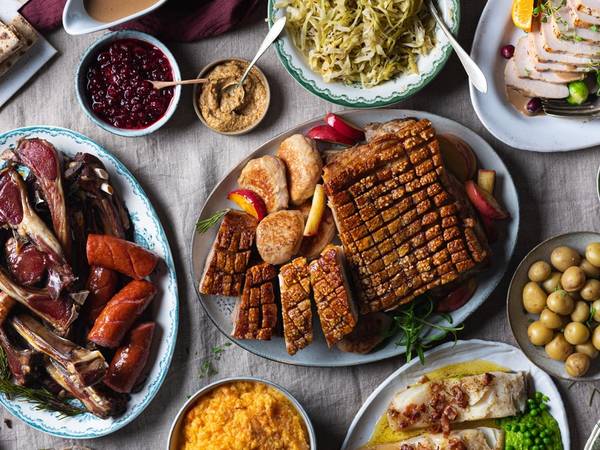 Et utvalg av tradisjonell julemat, inkludert ribbe, medisterkaker, surkål, grønnsaker og julepølser, på et dekket bord.