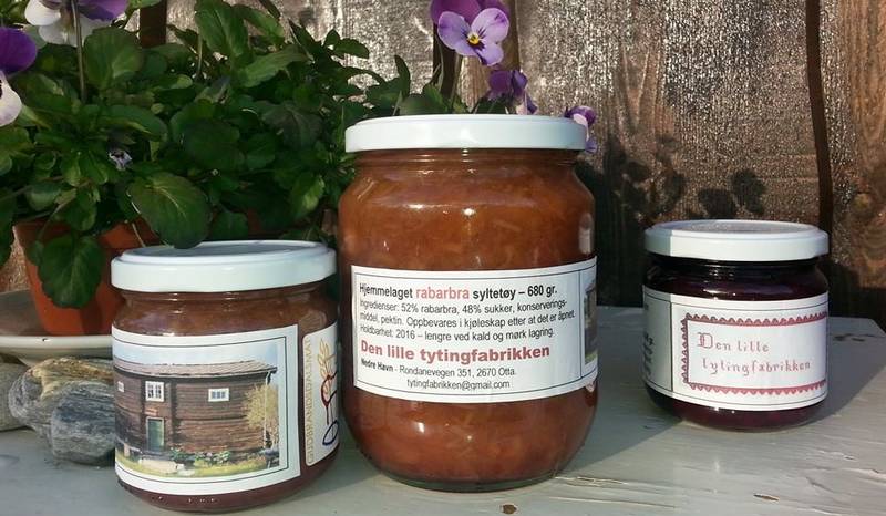 Rabarbrasyltetøy i glasskrukker med etiketter, plassert på en hylle med blomster i bakgrunnen.