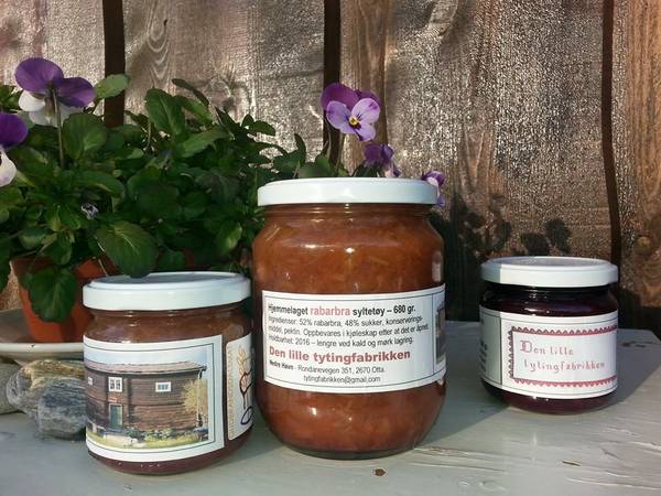 Rabarbrasyltetøy i glasskrukker med etiketter, plassert på en hylle med blomster i bakgrunnen.