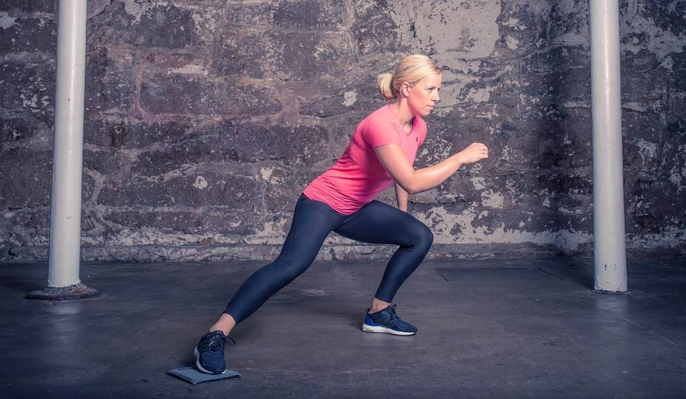 En person i rosa treningtøy gjør utfall foran en murvegg med sklimatte, klar for trening eller øvelse.
