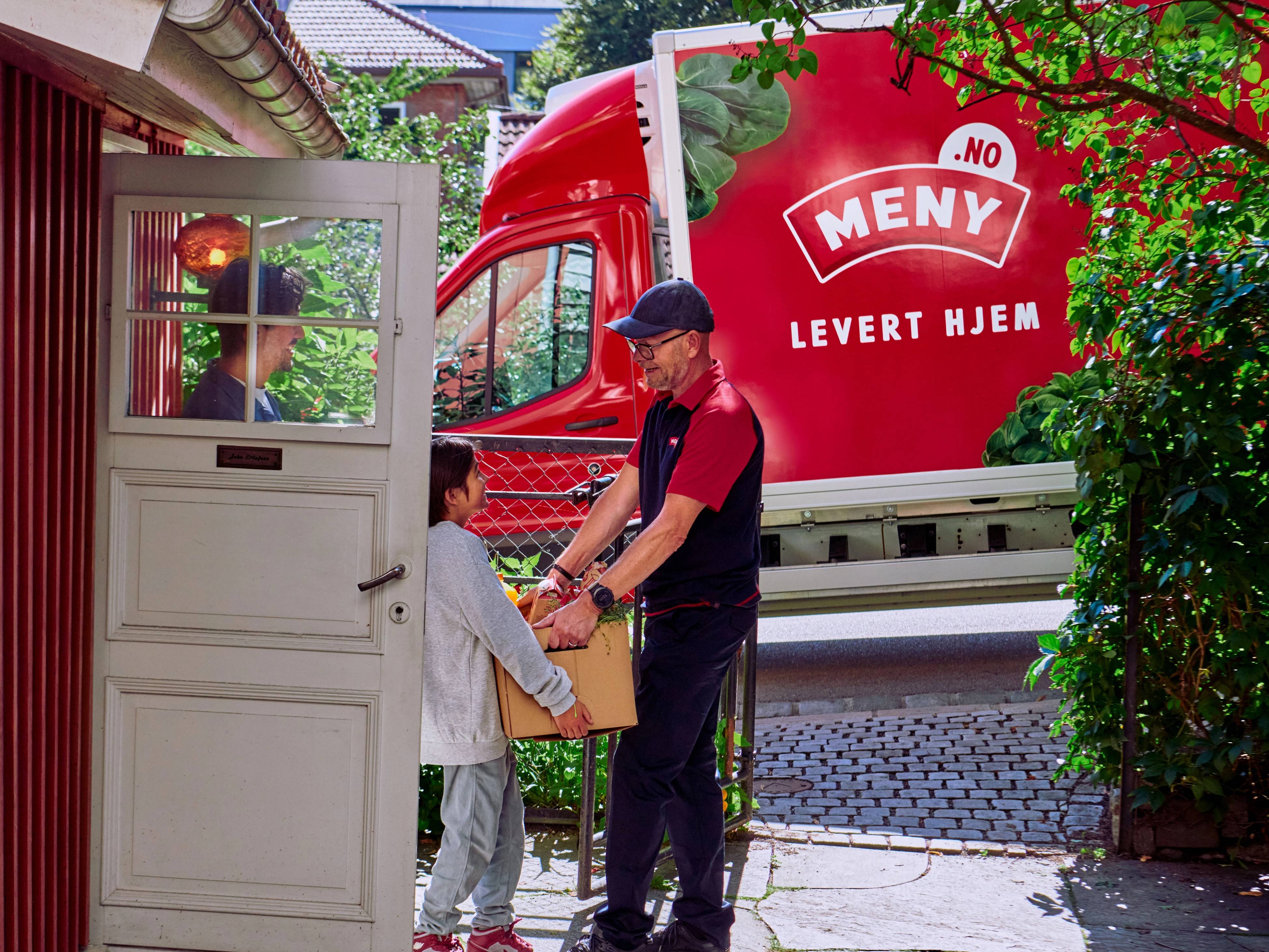 En mann i uniform leverer mat til to barn utenfor et hus, med en rød Meny-leveringsbil i bakgrunnen.