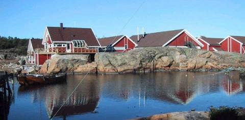 Fargerike hus langs vannet med en stor stein i forgrunnen, sett fra øst.