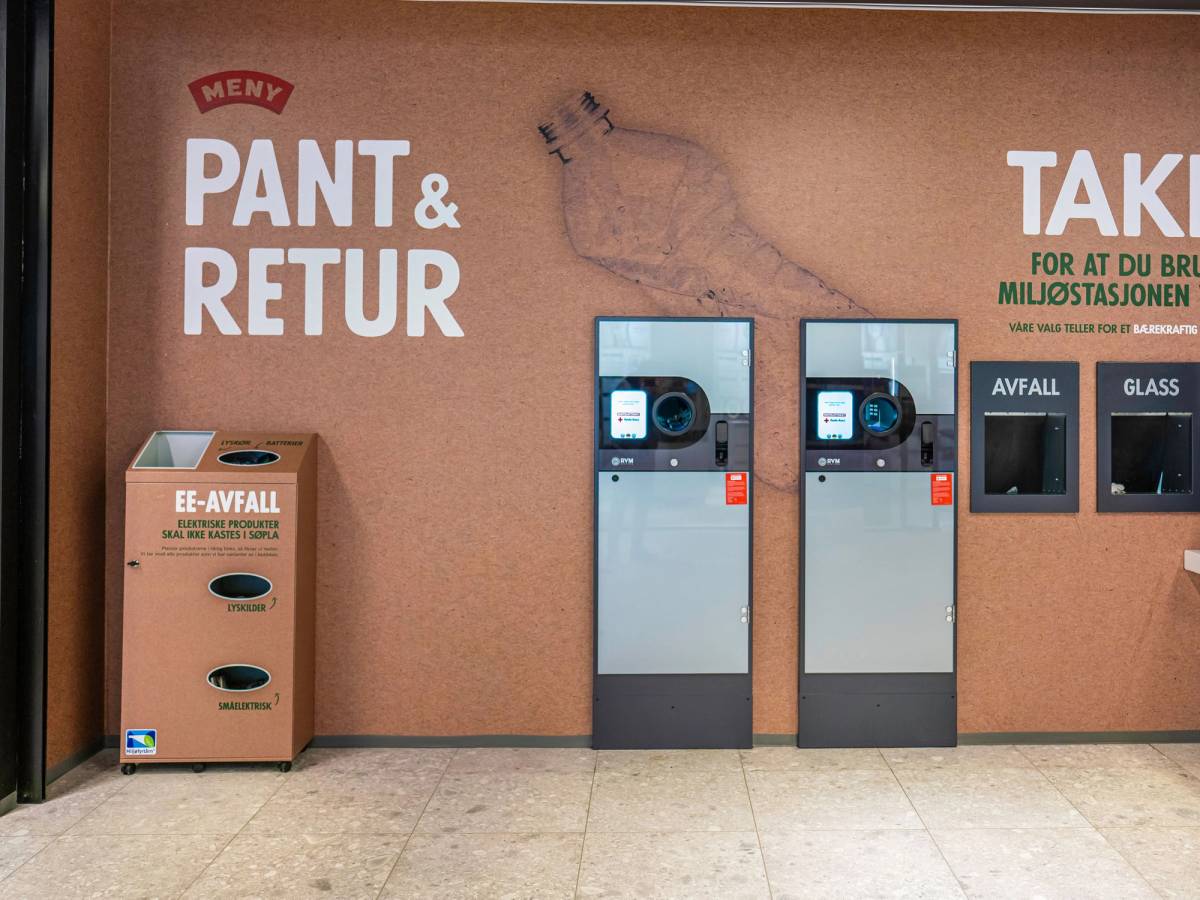 To vaskemaskiner står ved et returpunkt for klær, med en avfallscontainer til klær til venstre og informasjonsskilt til høyre.