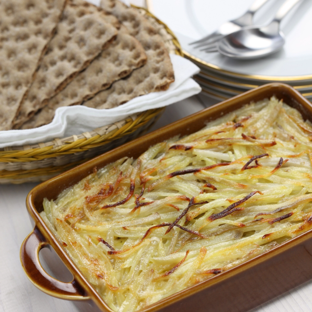 Janssons frestelse i en ildfast form med flatbrød ved siden av, på et bord med sølvbestikk i bakgrunnen.