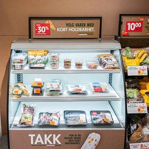 Nedpriste varer i en frysedisk med et skilt som tilbyr kort holdbarhet, og en annen plakat med 30 % rabatt, i en dagligvarebutikk.