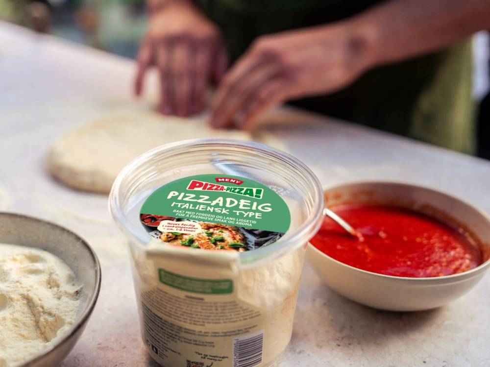 Person lager pizza med ferdig pizzadeig og tomatsaus på kjøkkenbenk.